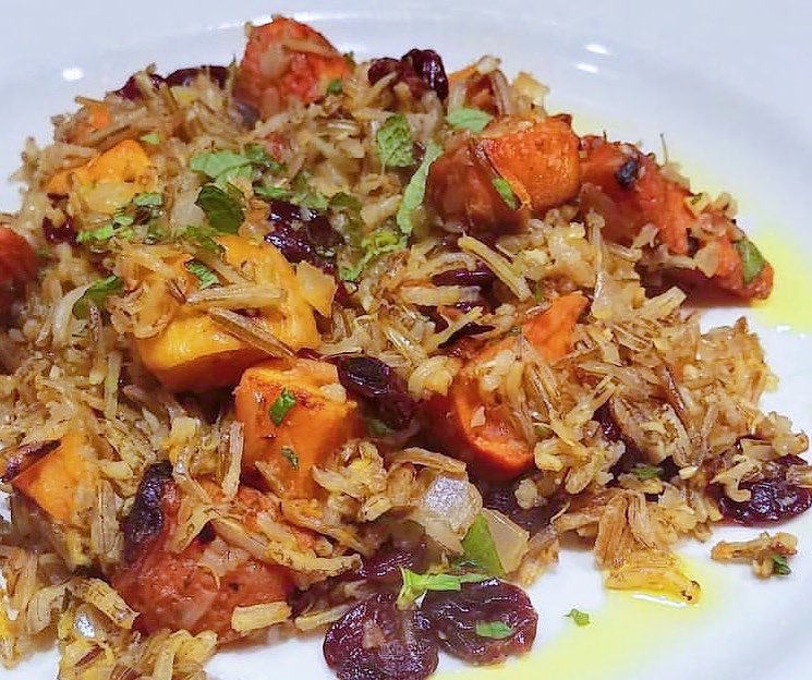 Wild rice with harvest vegetables like dried cranberries, squash and sweet potato plated on a bright white plate