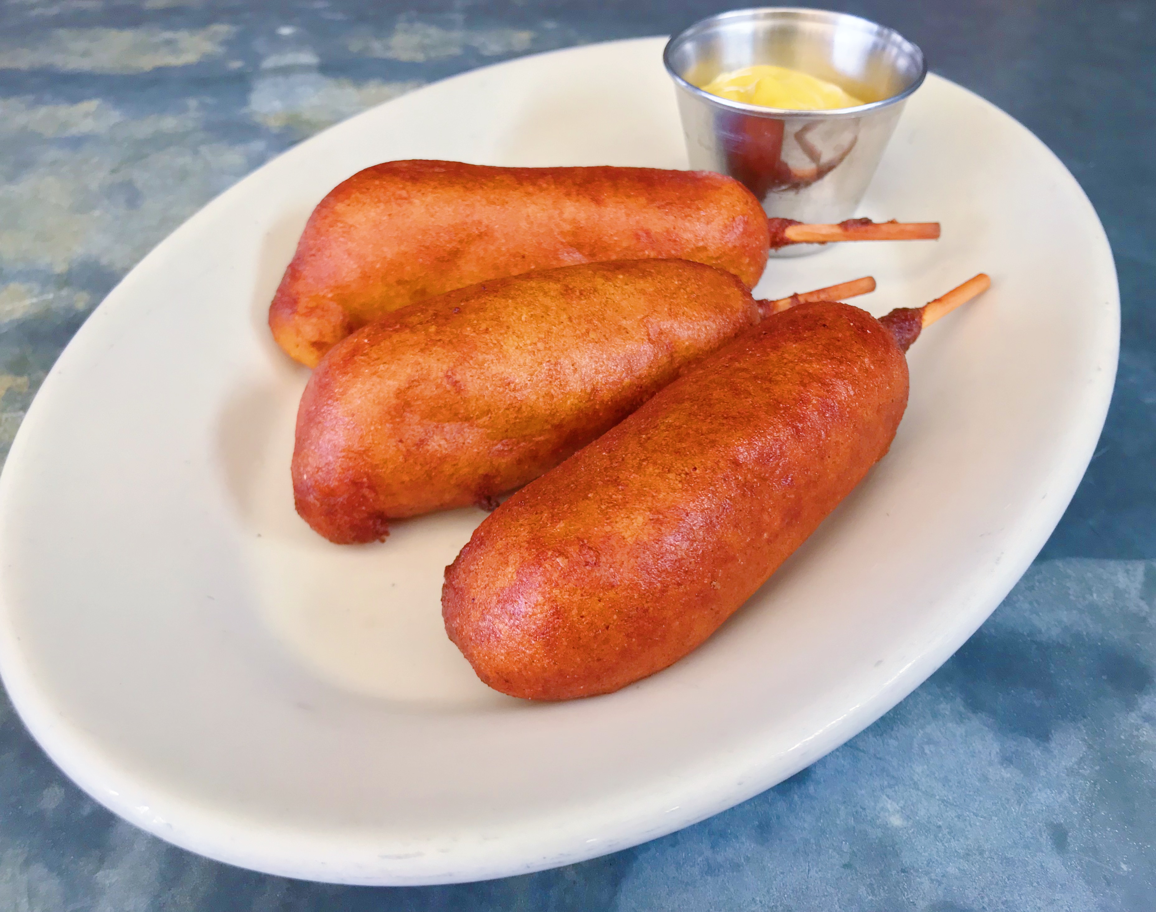 Plate of three corn dogs with a side of yellow mustard.