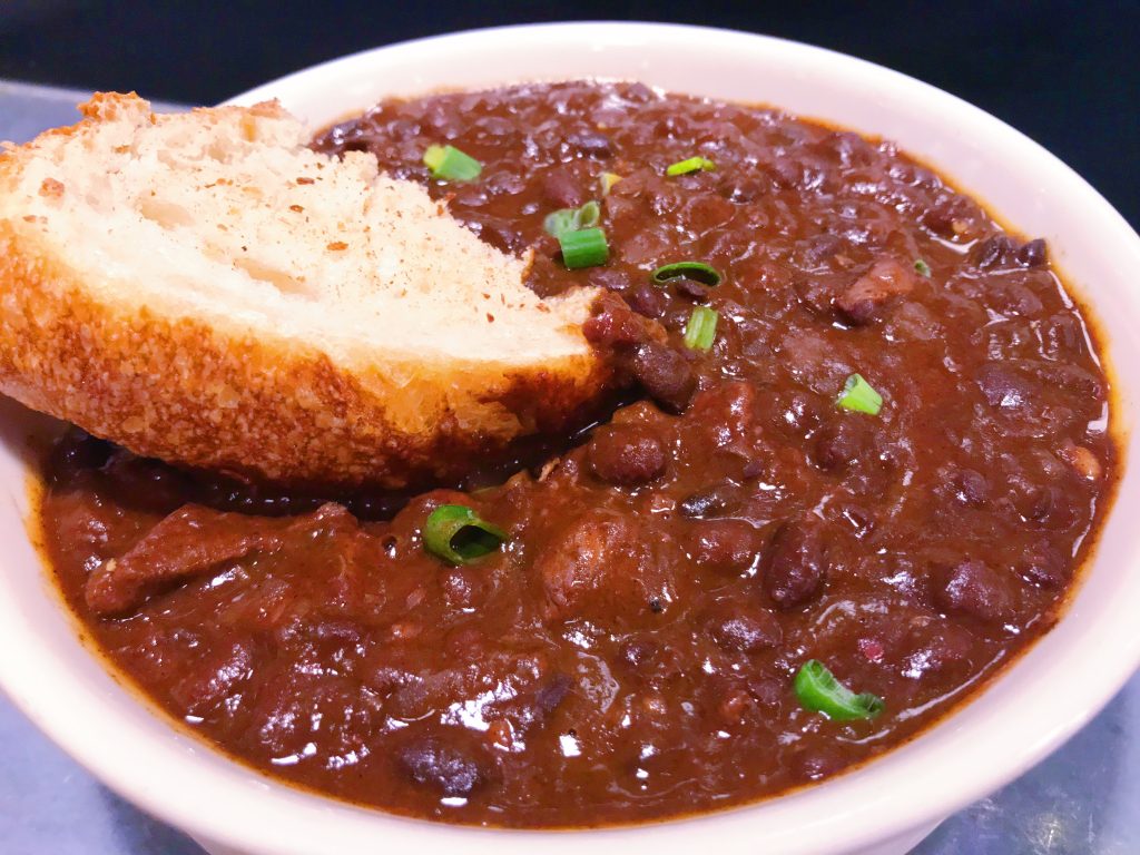 A bowl of Ancho Beef Chuck Chili with a piece of Bakehouse Sourdough bread.