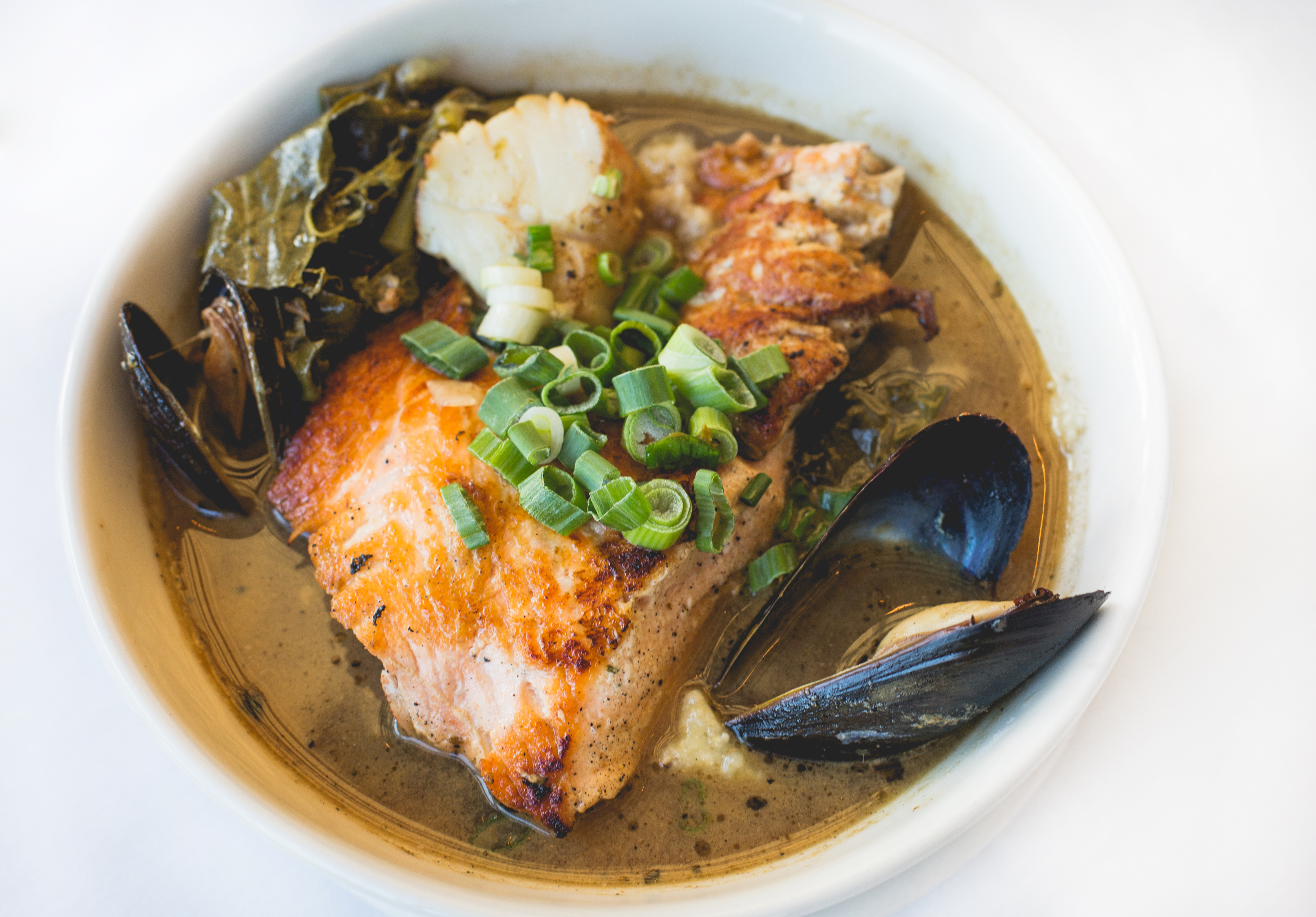 A bowl of Creole Potlikker Fish Stew with fish, mussels, scallops, greens, and grits.