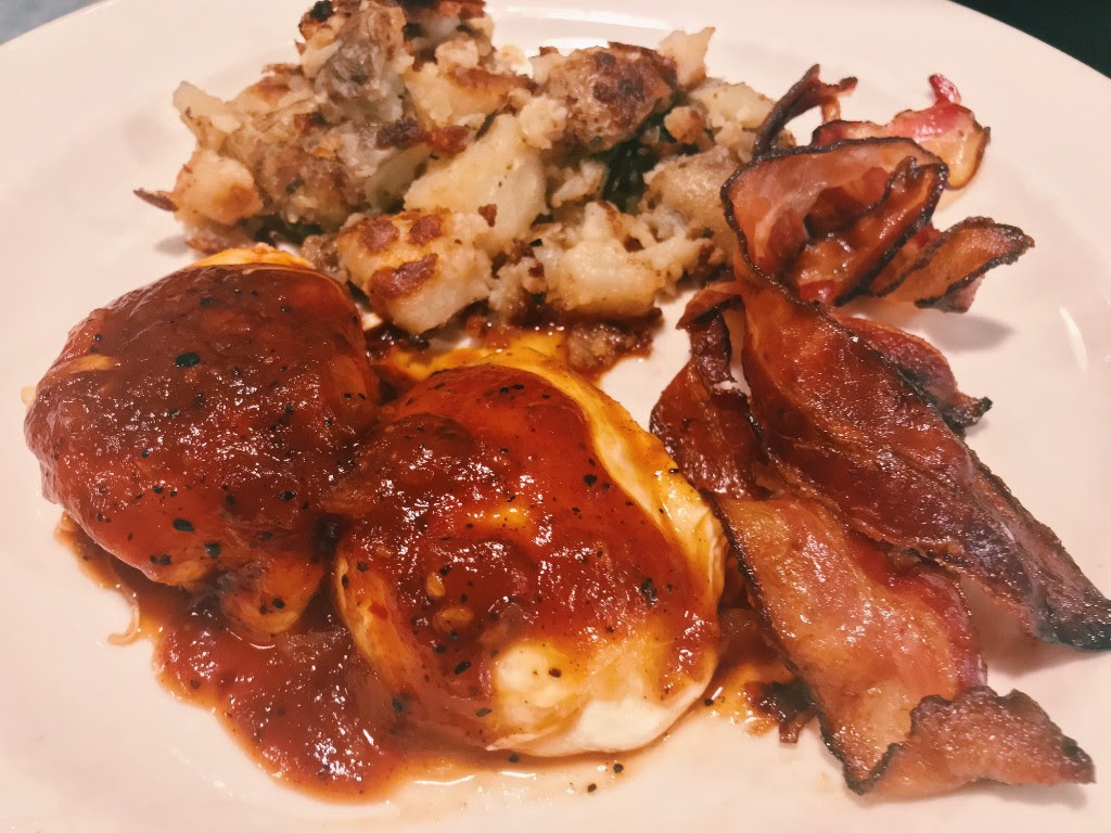 Poached eggs smothered in Red Rage BBQ sauce, with breakfast potatoes and bacon.