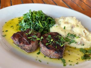 A plate with grilled steak, mashed potatoes, and spinach, drizzled with olive oil