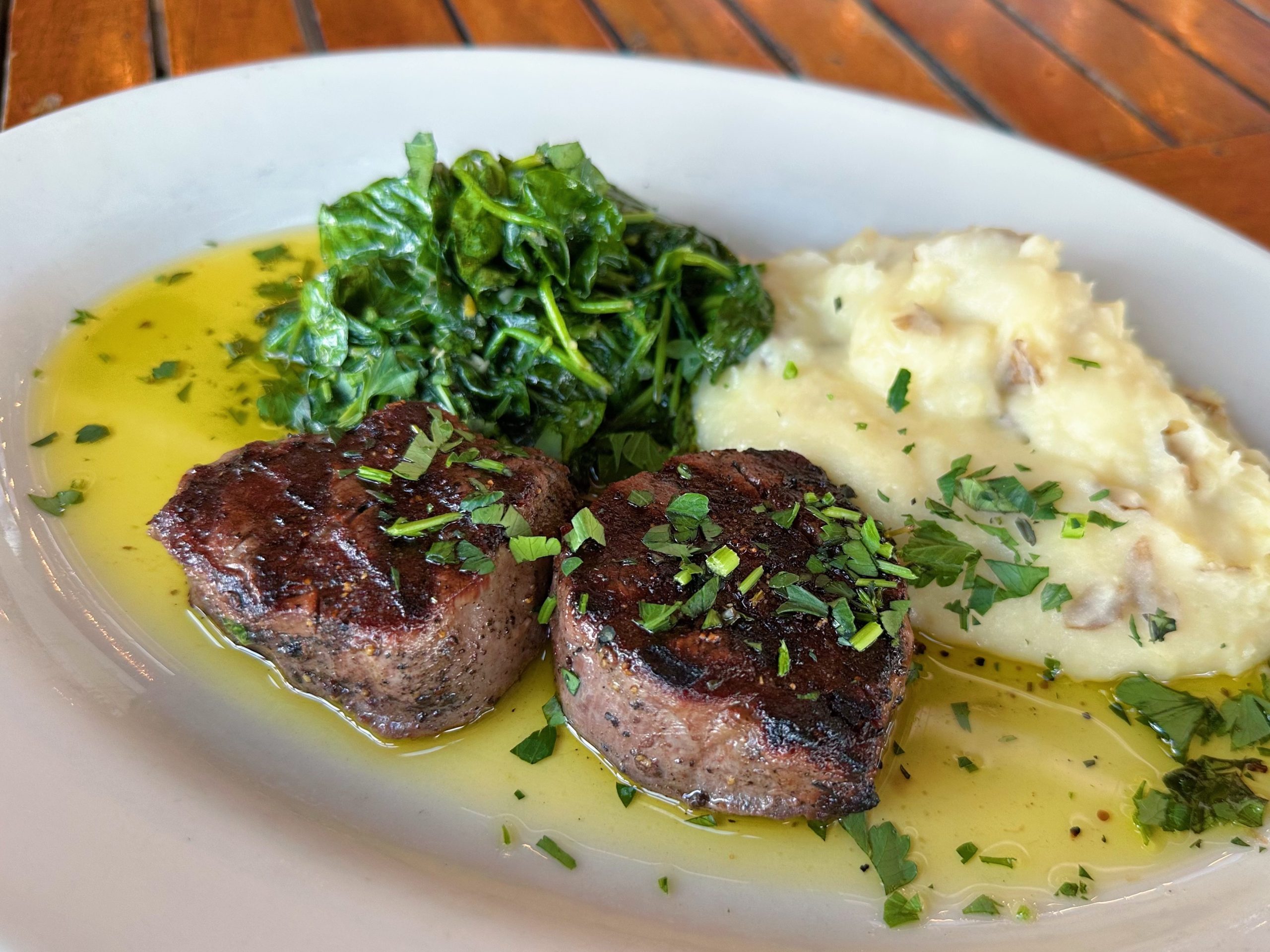 A plate with grilled steak, mashed potatoes, and spinach, drizzled with olive oil
