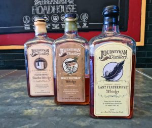 In order of the flight, bottles of whiskey from Journeyman Distillery: Featherbone Bourbon, Buggy Whip Wheat, and Last Feather Rye.