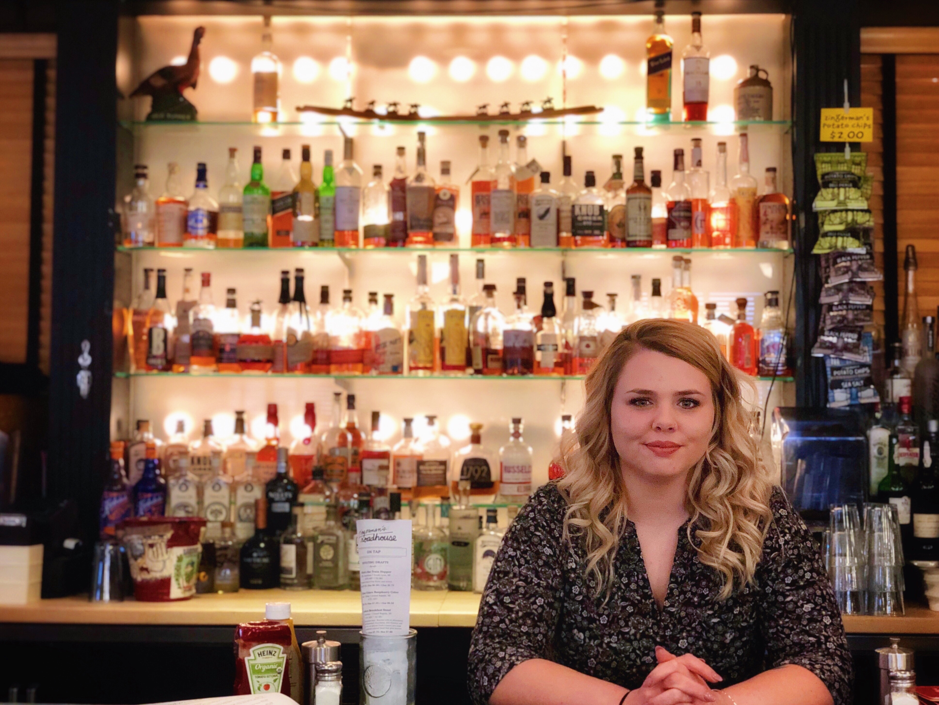 Roadhouse Bar Manager, Sarah Bartlett, in front of shelves of whiskey and bourbon.