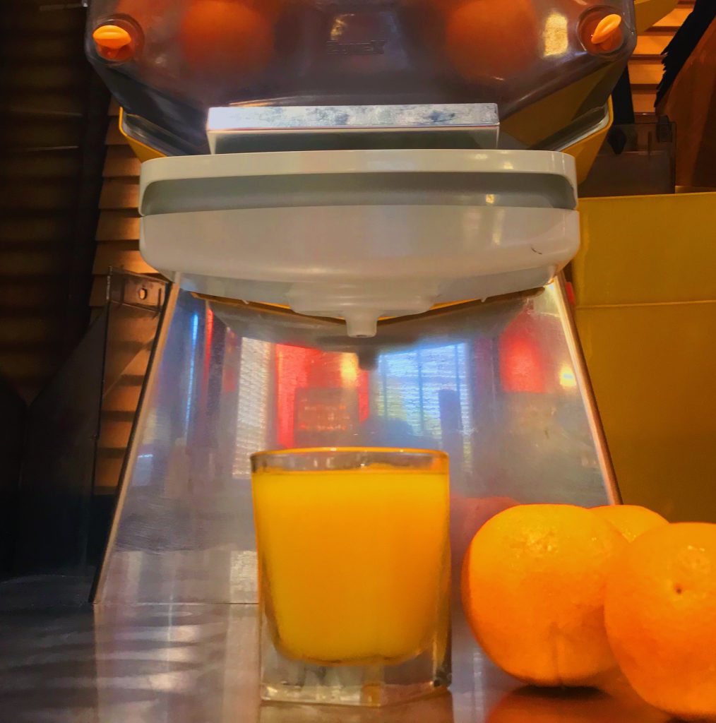 A glass of freshly squeezed orange juice in front of a large, state of the art juicer at the Roadhouse.