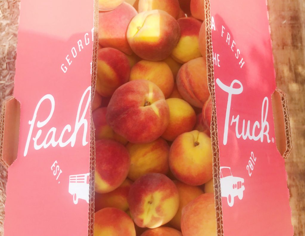 A box of peaches with the Peach Truck logo on the top, opened to reveal the peaches inside.