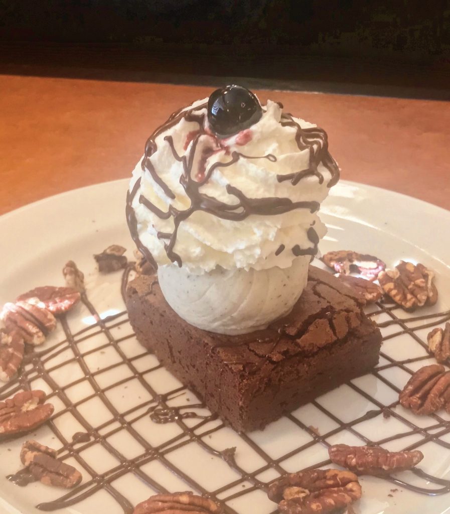 A Roadhouse brownie sundae with vanilla gelato, whipped cream, a Maraschino cherry, and chocolate sauce.