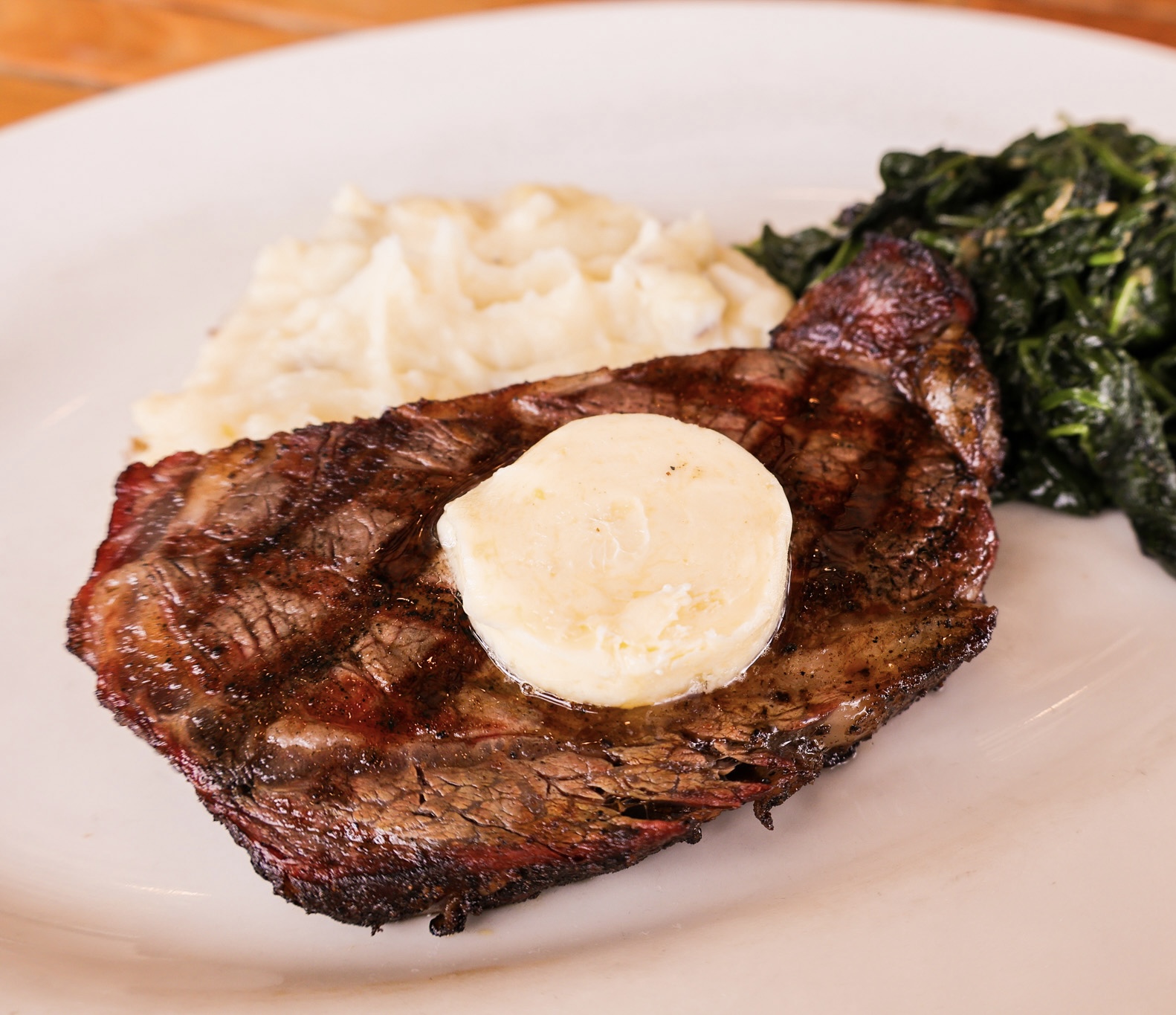 A grilled ribeye topped with butter, plated with mashed potatoes and spinach.