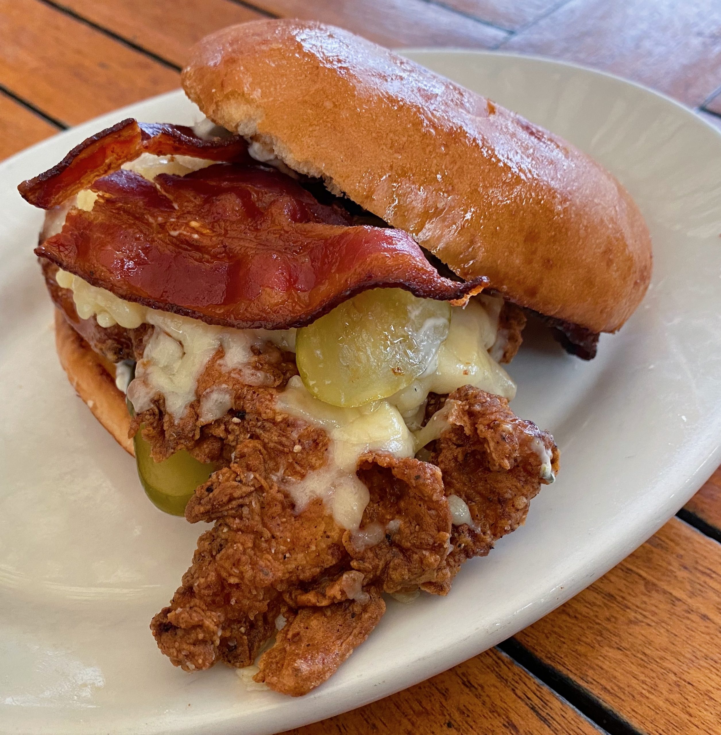 A fried chicken sandwich with pickles, bacon, and cheddar cheese.