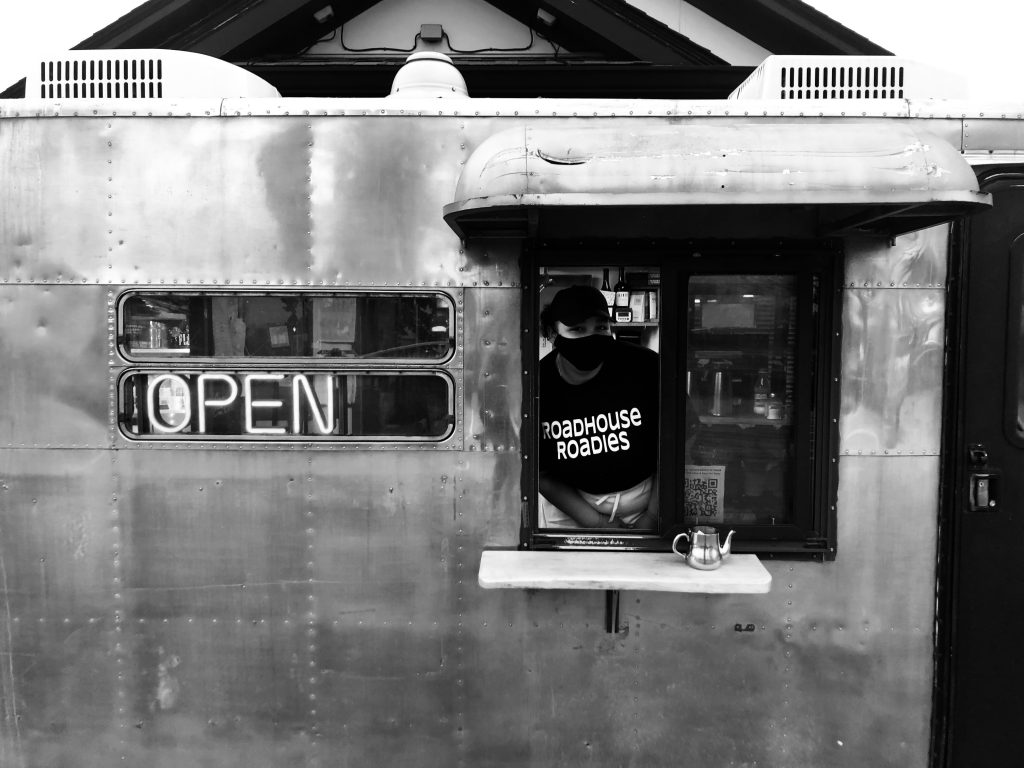 A masked Roadhouse employee stands in the window of the Roadshow, with the Open sign lit up next to her.