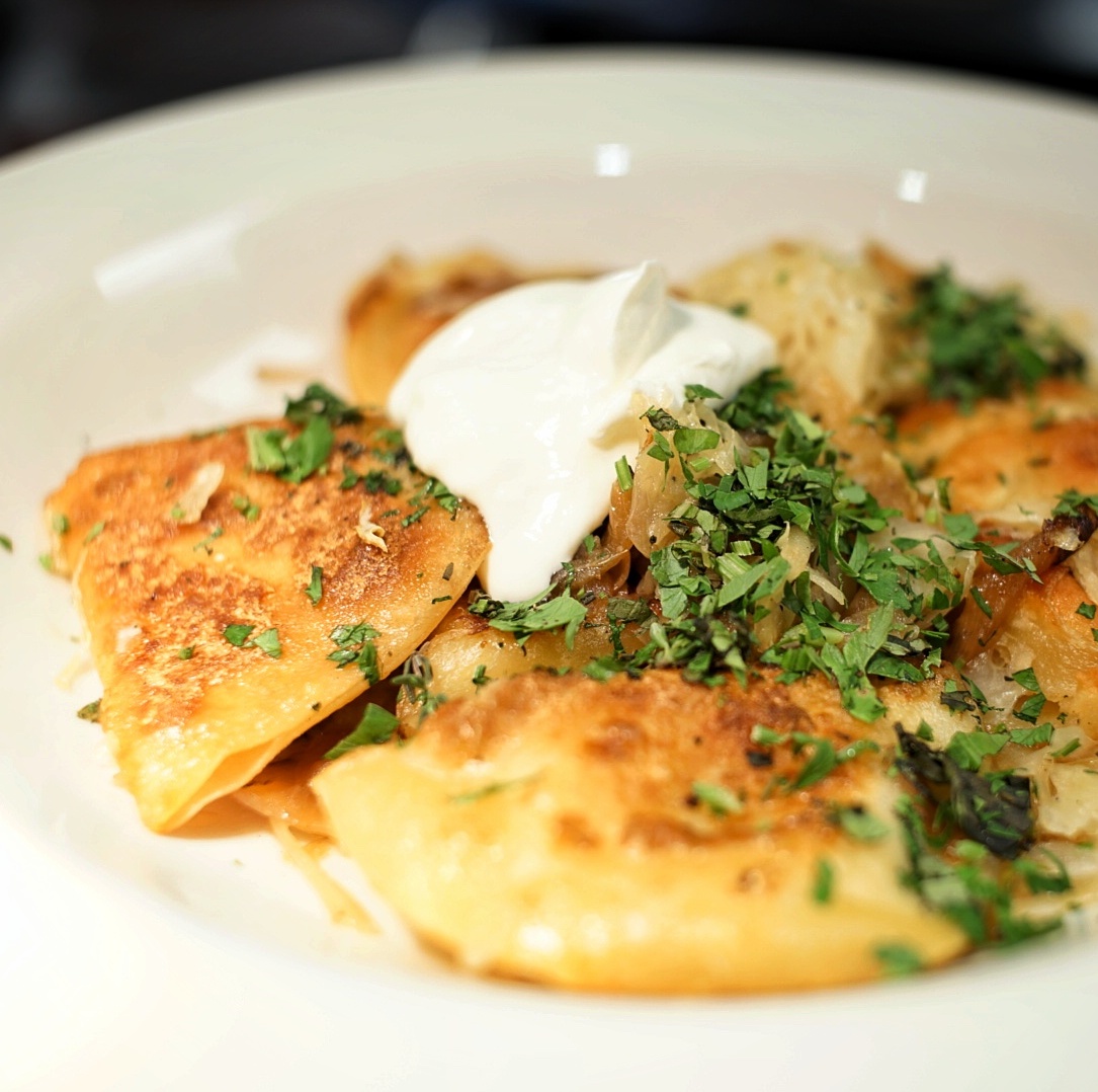 A plate of potato pierogi with sour cream.