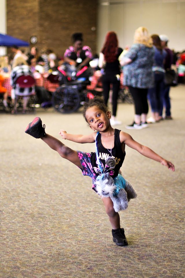 A little girl smiles and kicks her leg up in joy.