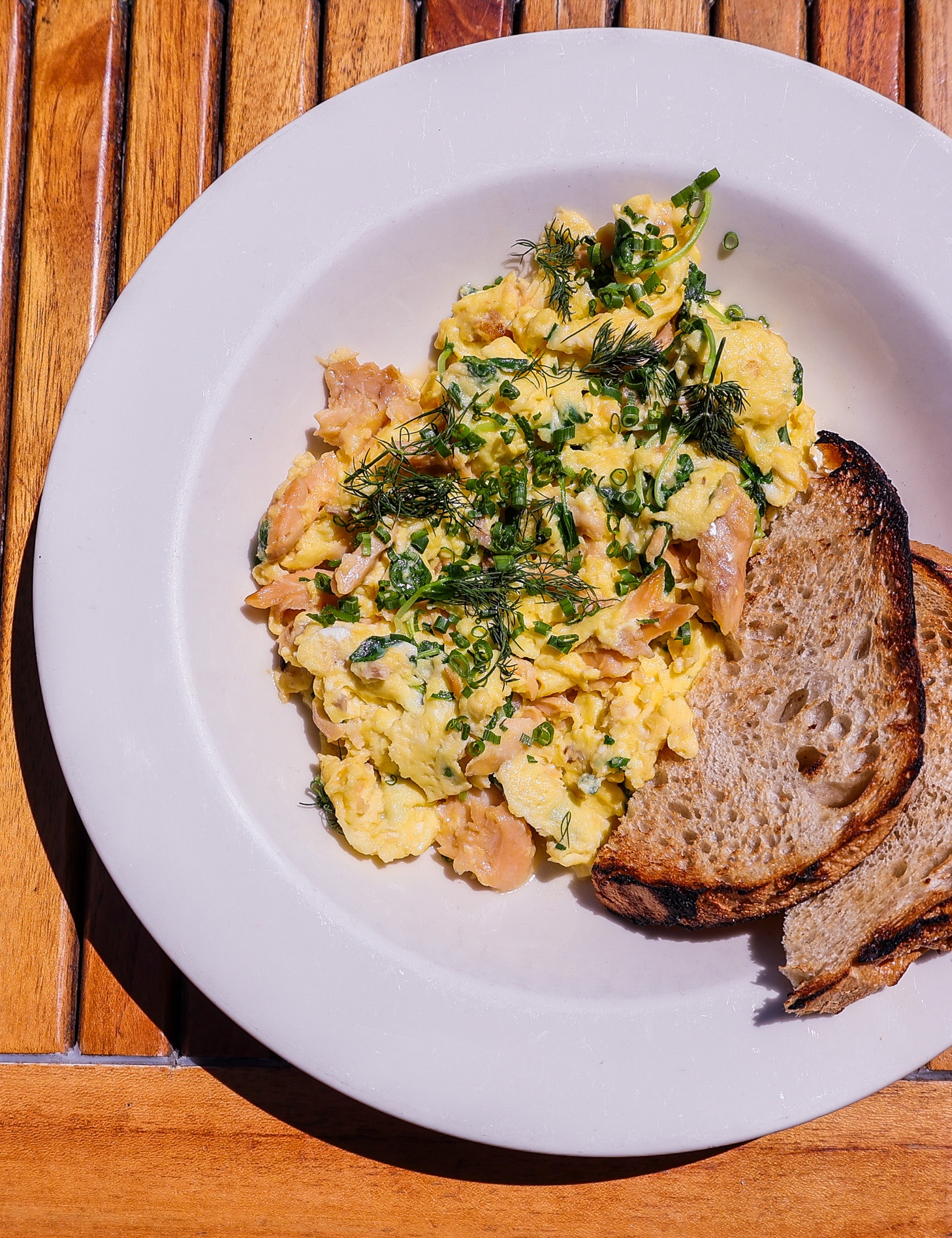 A plate full of scrambled eggs, smoked trout, and toast.