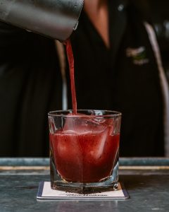 A bartender pours a dark red cocktail into a rocks glass.