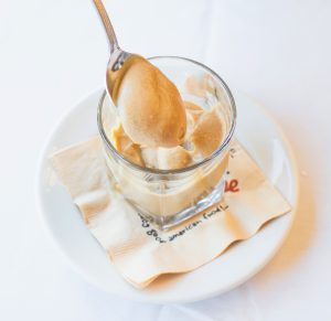 A glass full of creamy butterscotch pudding and a spoonful being lifted out.
