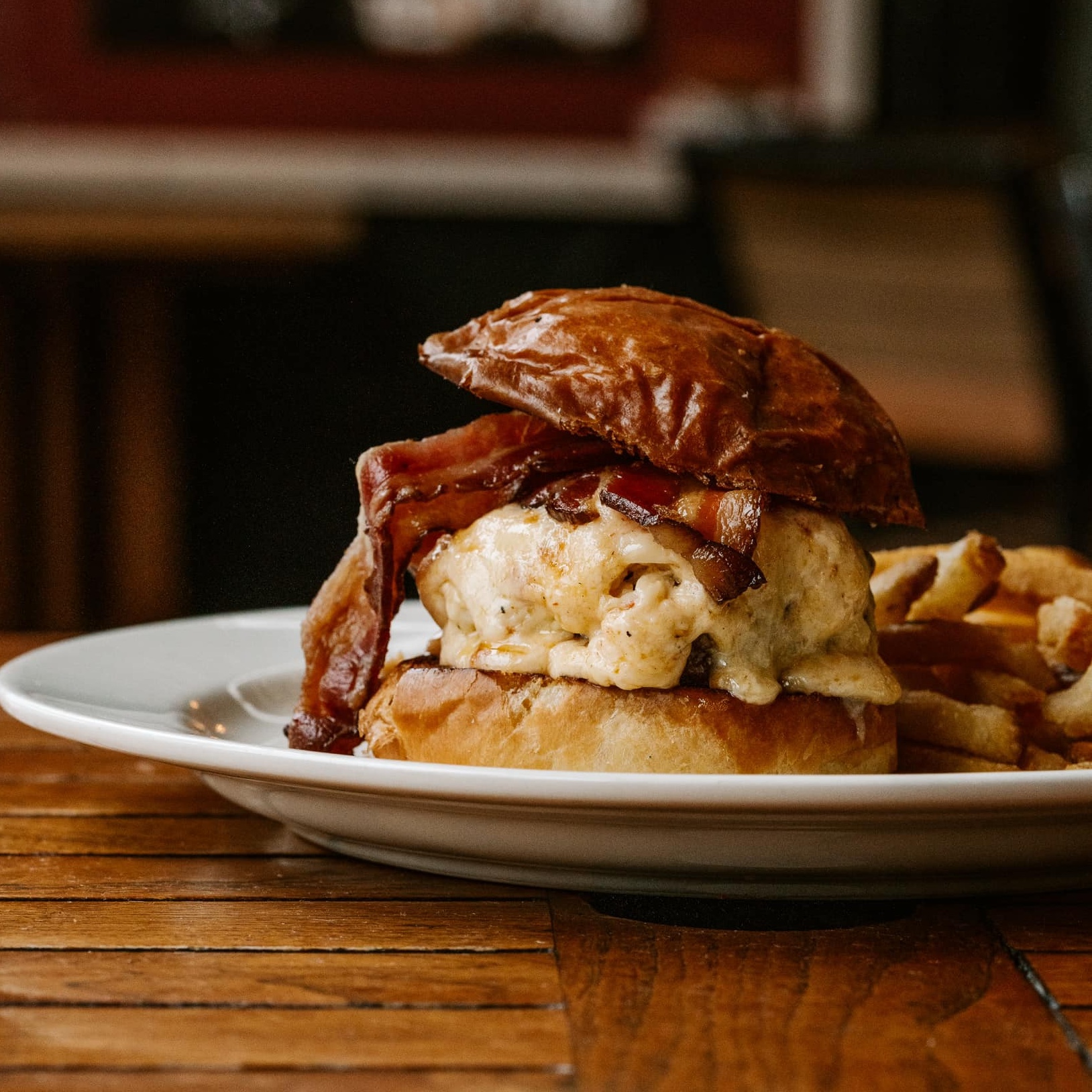 A side view of a burger topped with melted pimento cheese and bacon.