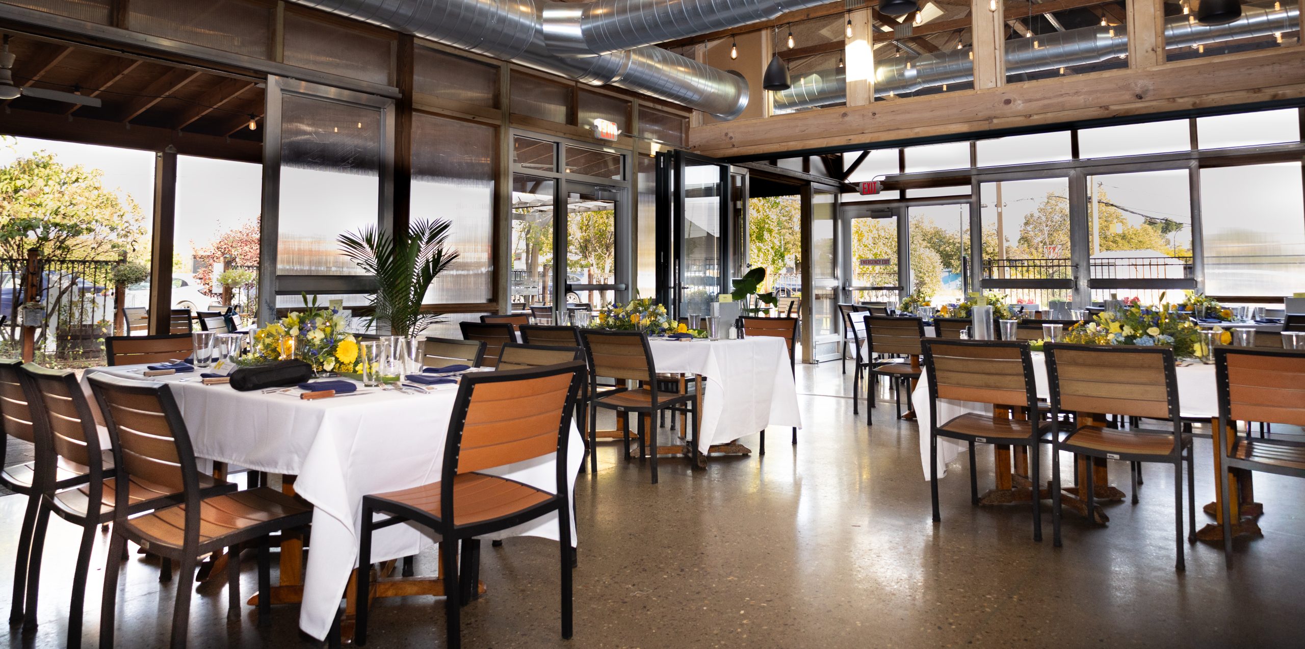 A view of a patio dining space with tables set with white linens and flowers
