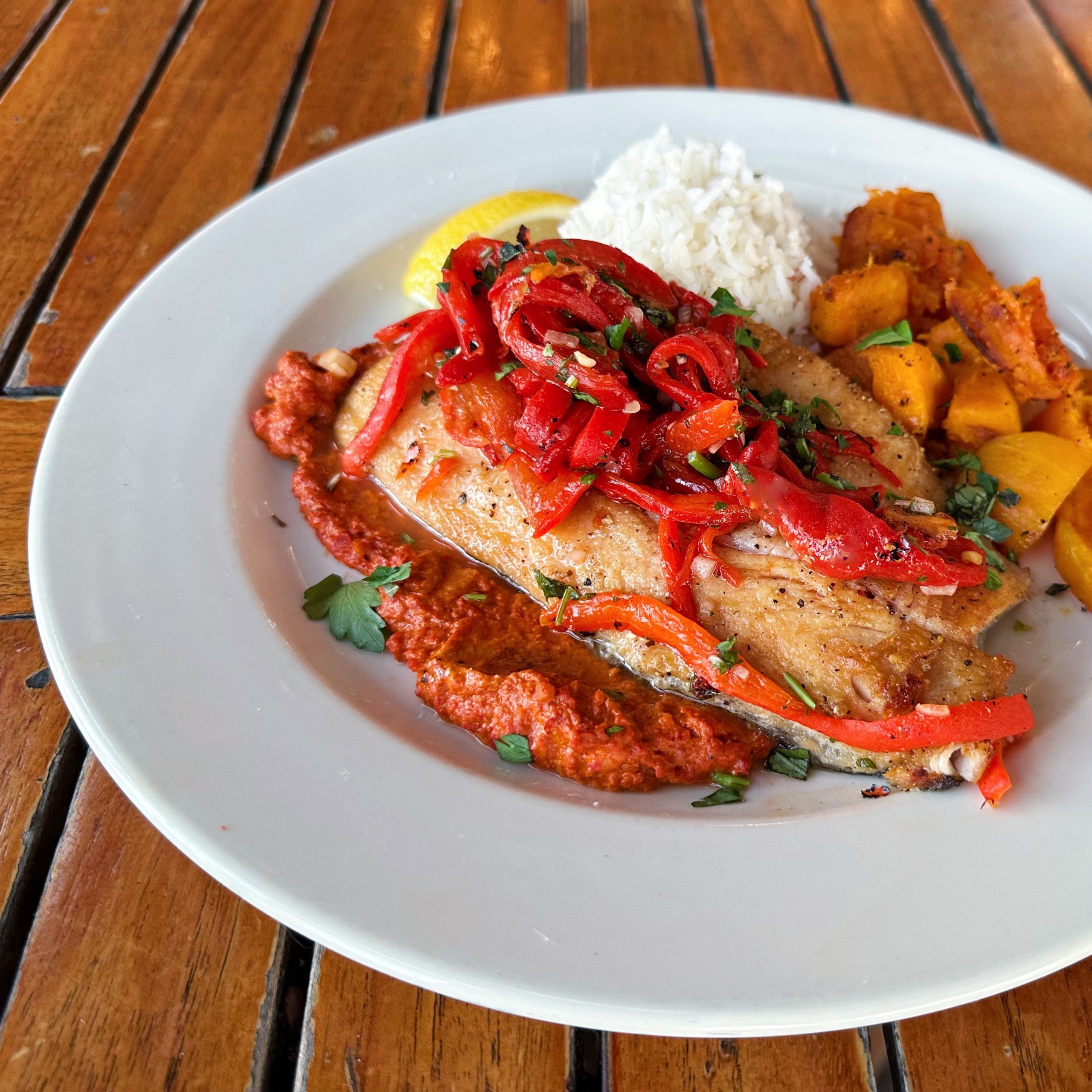 a rainbow trout dish topped with roasted red peppers, served on a red muhammara sauce.