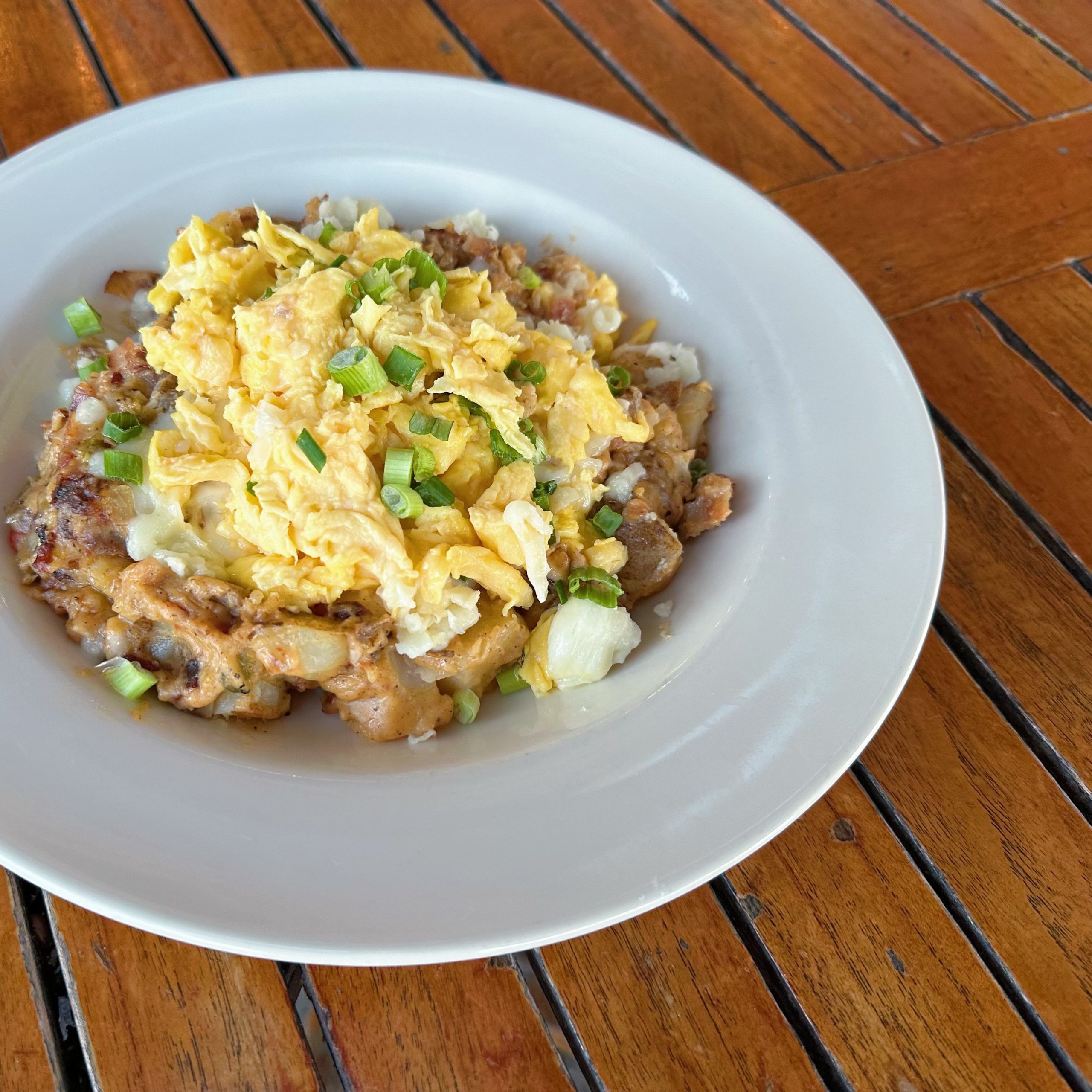 A breakfast bowl of scrambled eggs, breakfast potatoes, and green chili gravy.