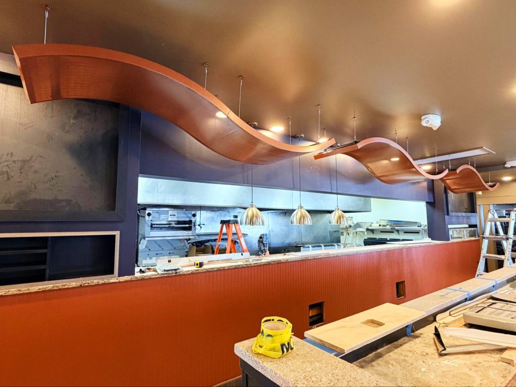 A photo of a kitchen line with curved copper baffles in front of the food window.
