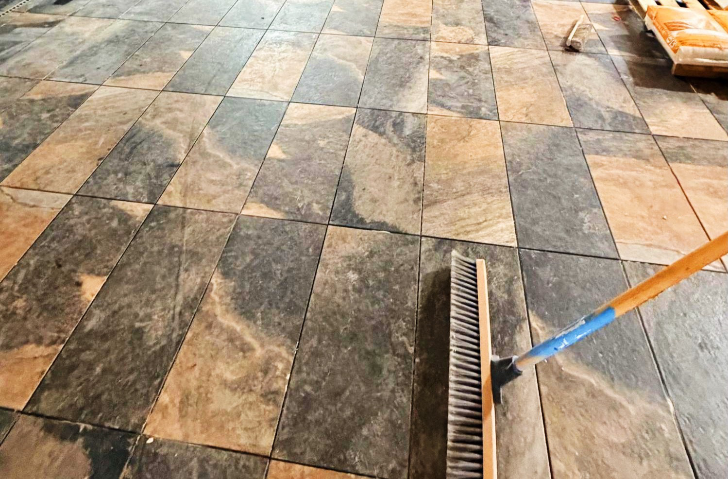 A ceramic tile floor
 with a broom in one corner.