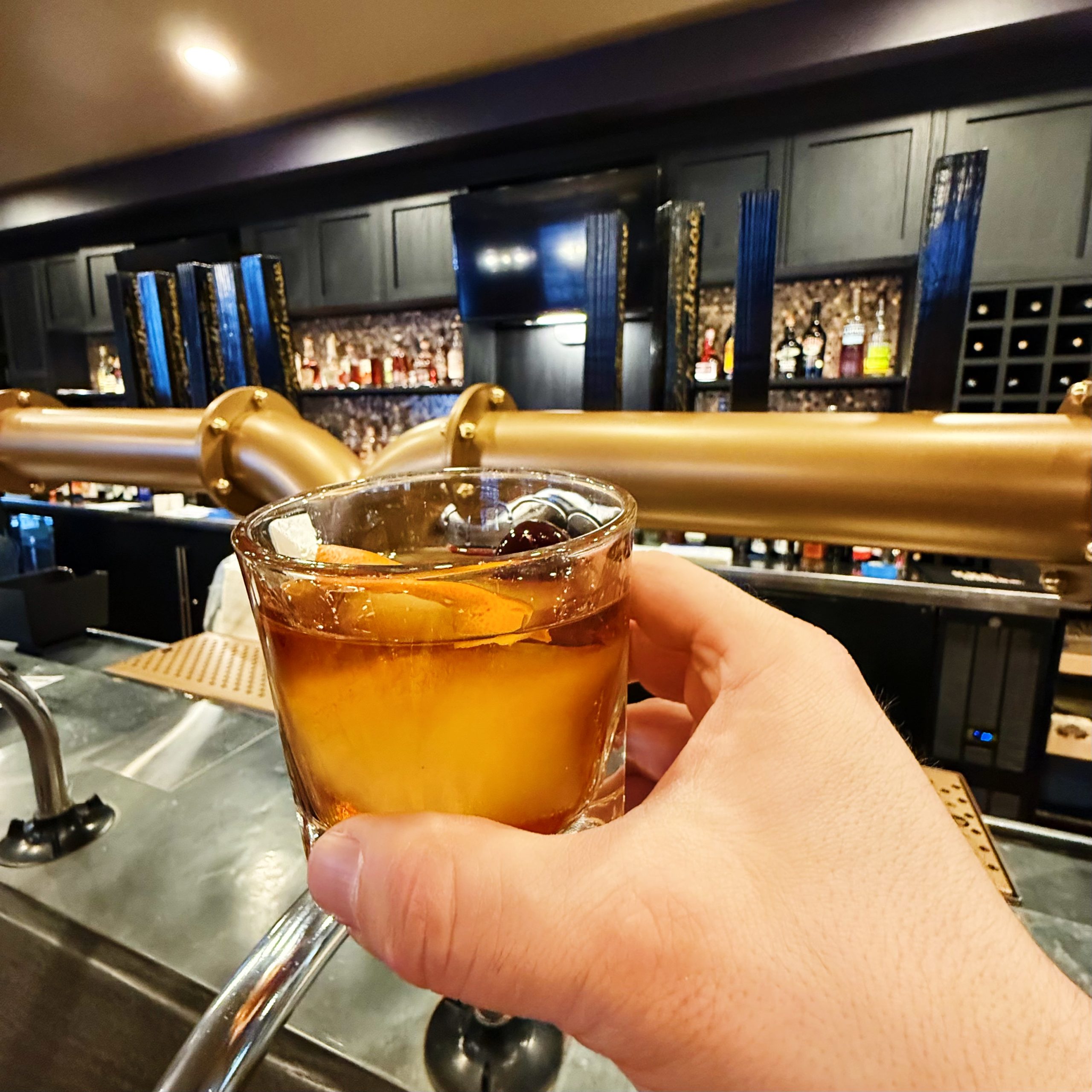 A hand holding up an Old Fashioned as a toast