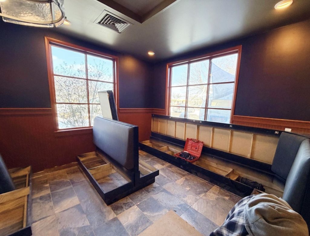 A dining room under construction, with a long booth installed that can seat a large group.