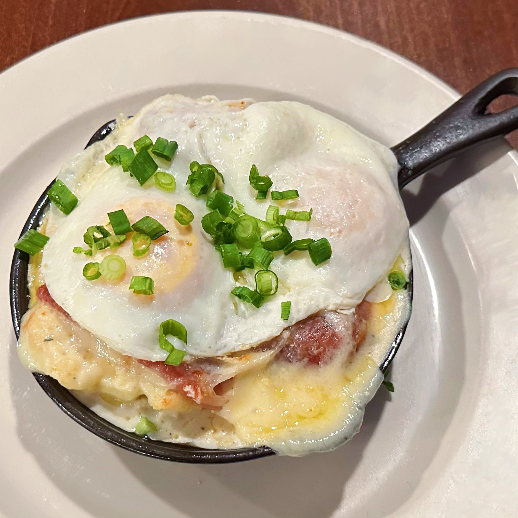 A personal cast iron skillet with biscuits topped with melted Swiss cheese, country ham, and two over easy eggs.