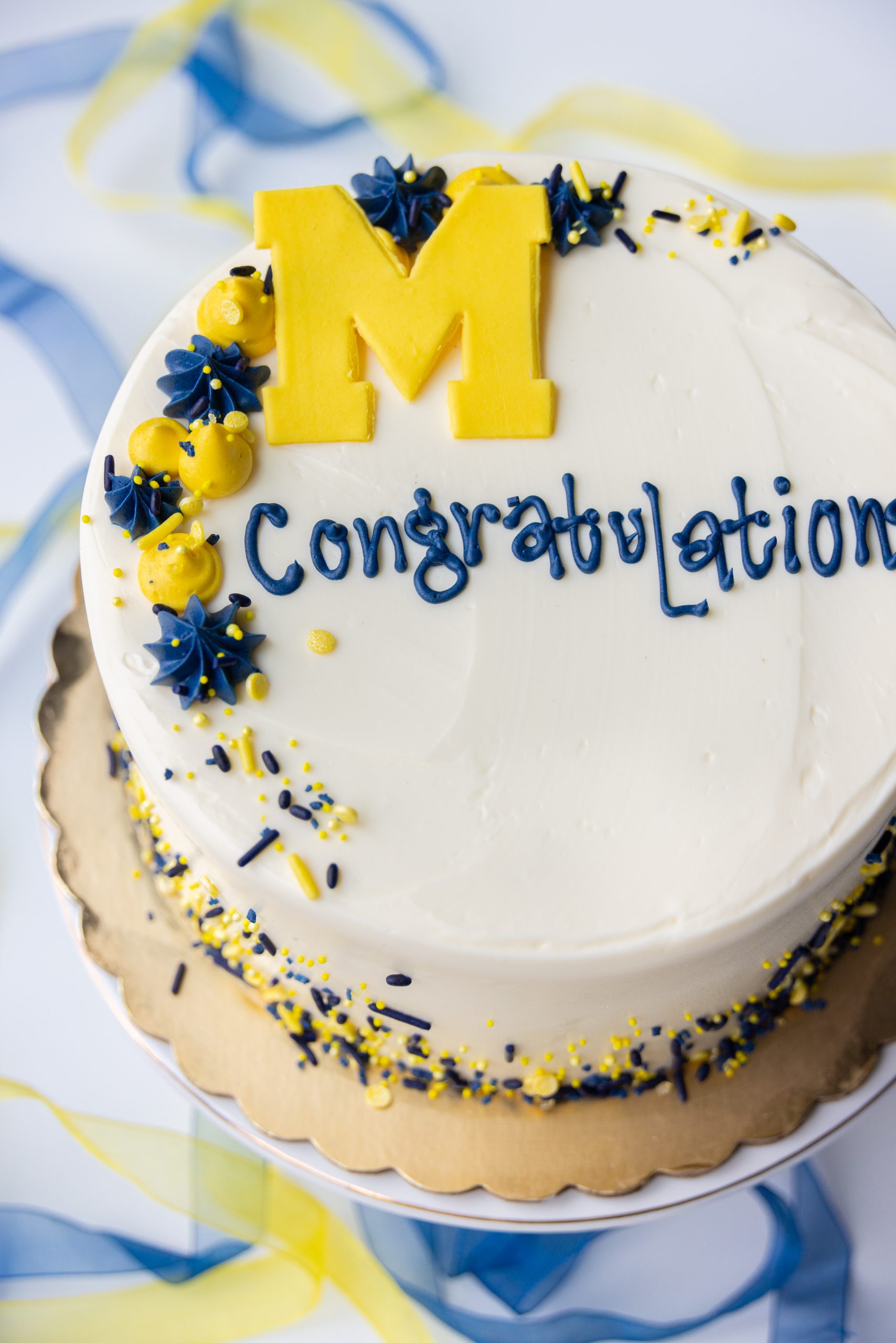 A graduation cake decorated with a yellow M for Michigan, and the words Congratulations piped in blue.