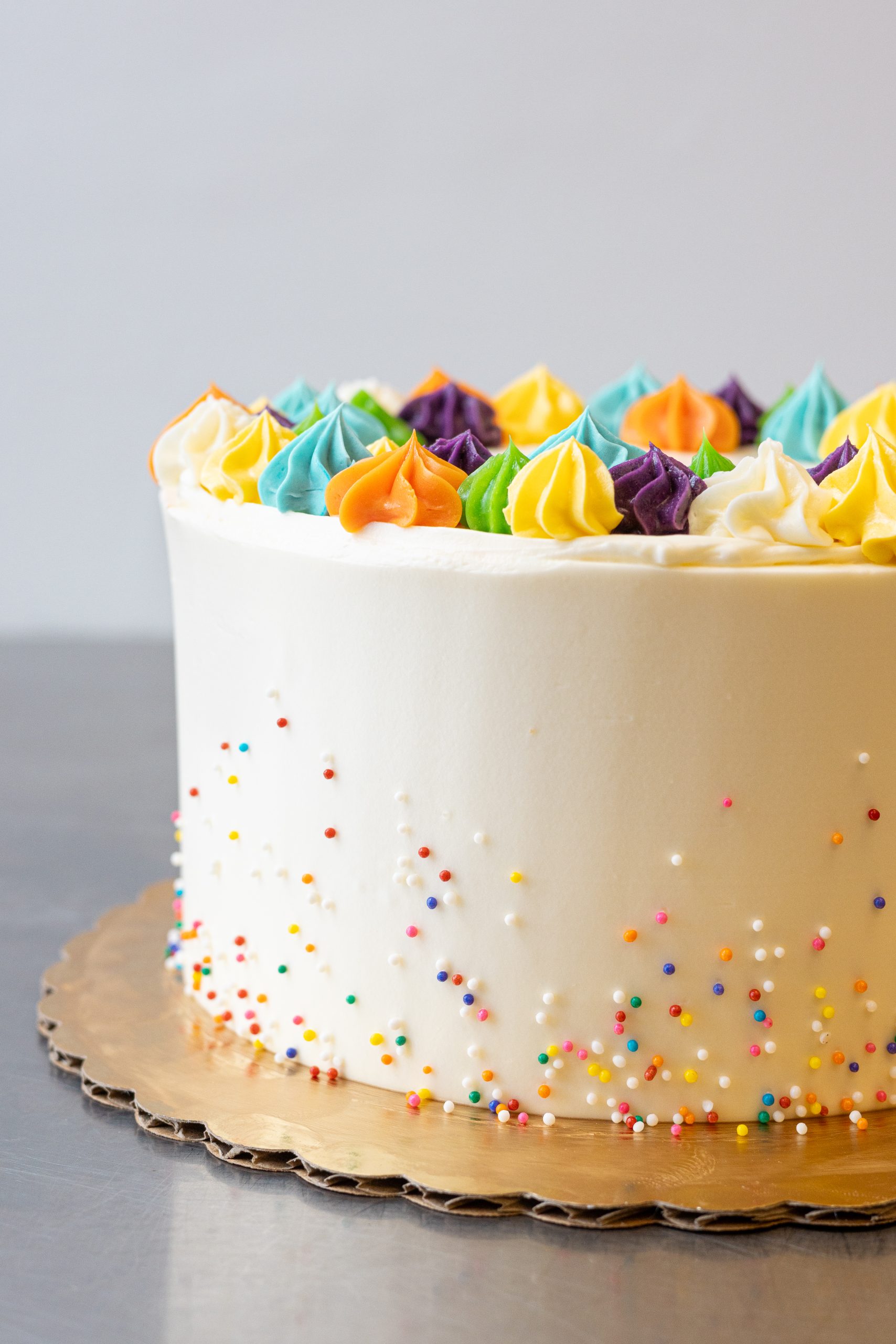 A white frosted cake with sprinkles on the side, topped with multicolored florettes.