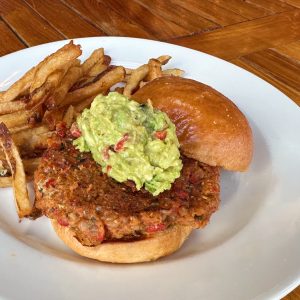 A vegetarian burger with a scoop of avocado salad on top.