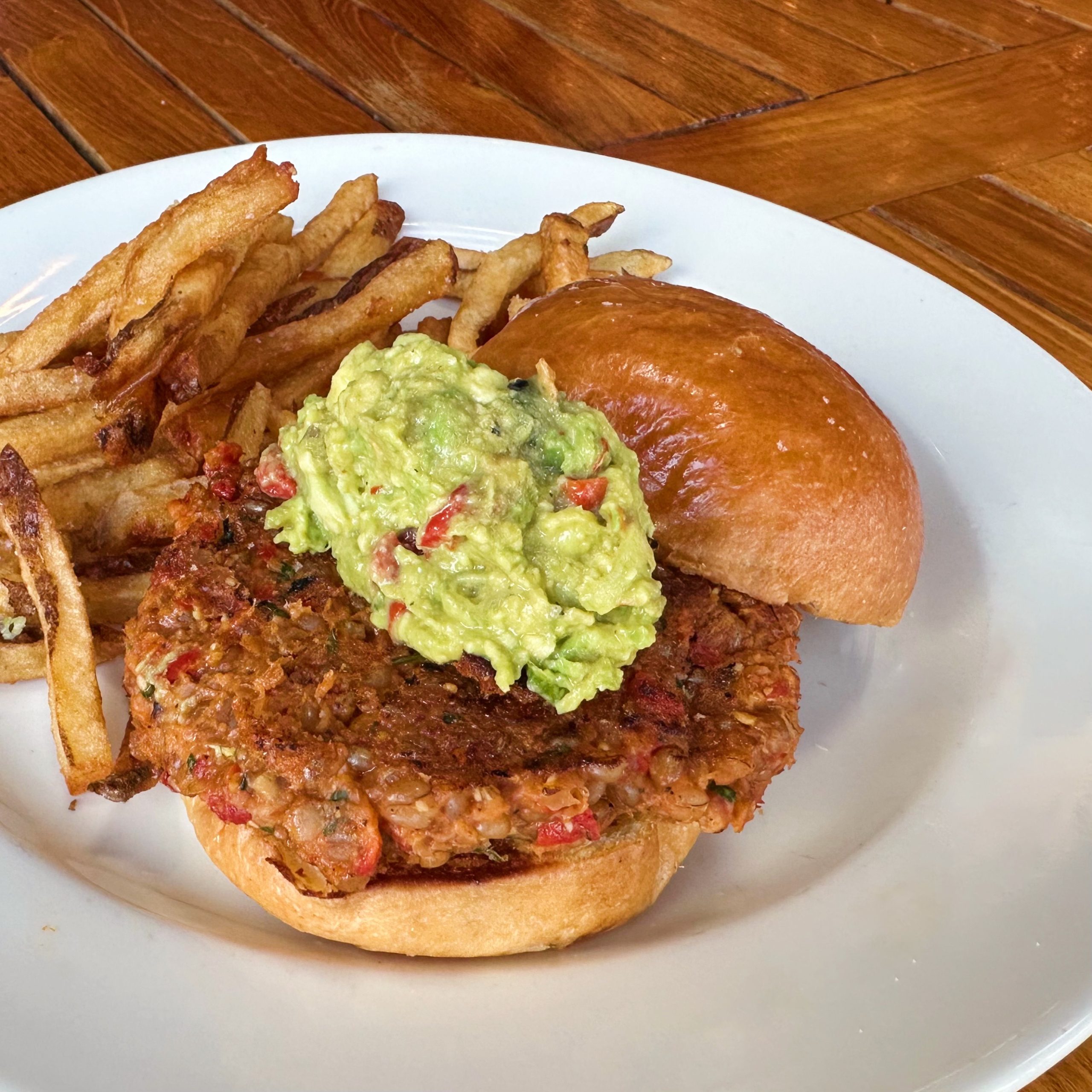 A vegetarian burger with a scoop of avocado salad on top.