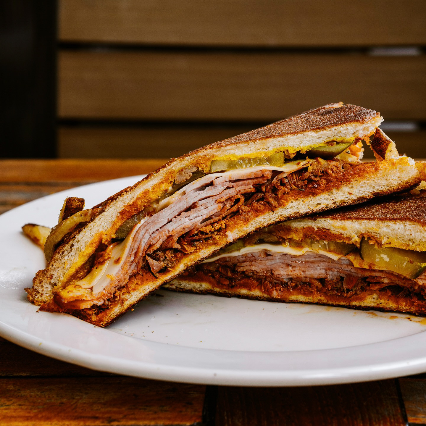 A Cuban sandwich cut open to reveal layers of smoked ham, melted cheese, pickles, and a red sauce.