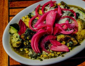 A plate of grilled zucchini, squash, tomatoes, and melted cheese, topped with pickled onions