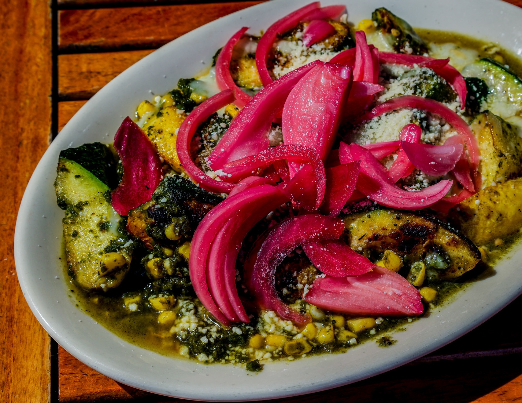 A plate of grilled zucchini, squash, tomatoes, and melted cheese, topped with pickled onions