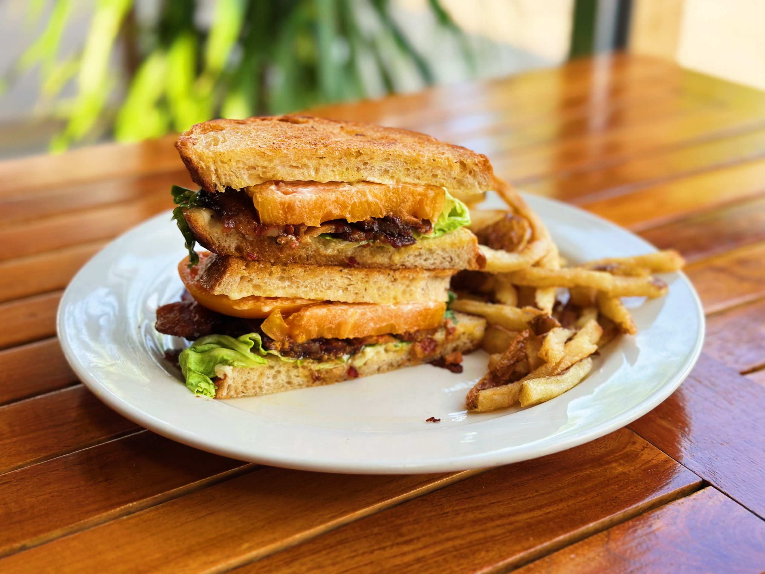 An heirloom tomato BLT cut open to reveal layers, plated up with fries.