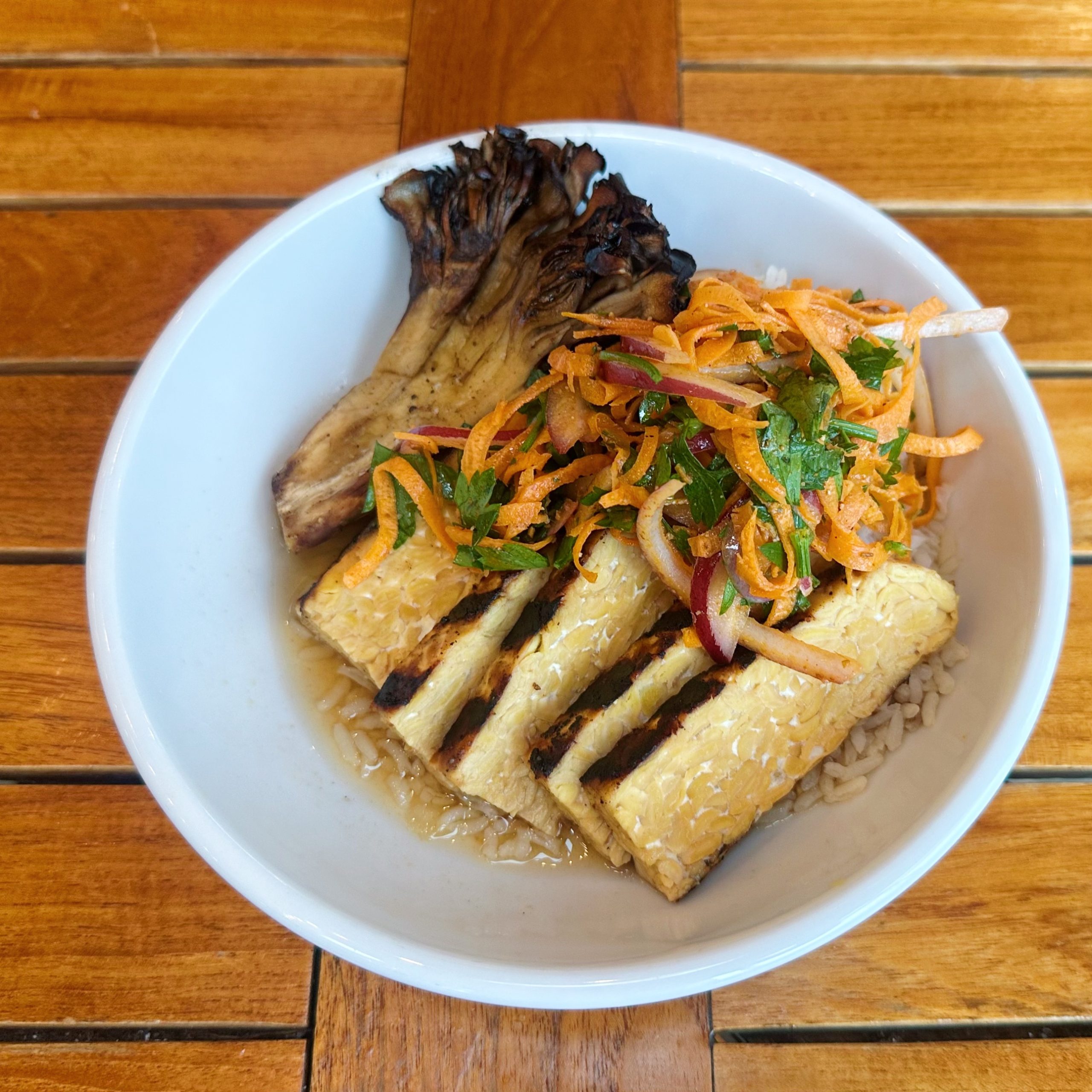 A bowl of sliced, grilled tempeh with maitake mushroom and a carrot slaw.