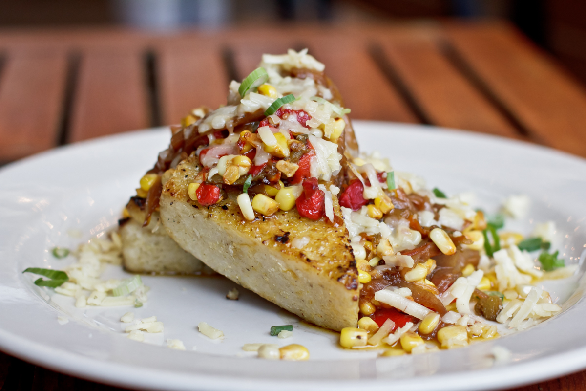 A plate of slcied grilled grits topped with corn, red pepper, and cheese.