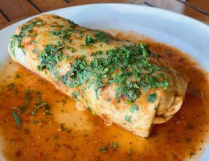 A burrito smothered in a red sauce and topped with chopped cilantro