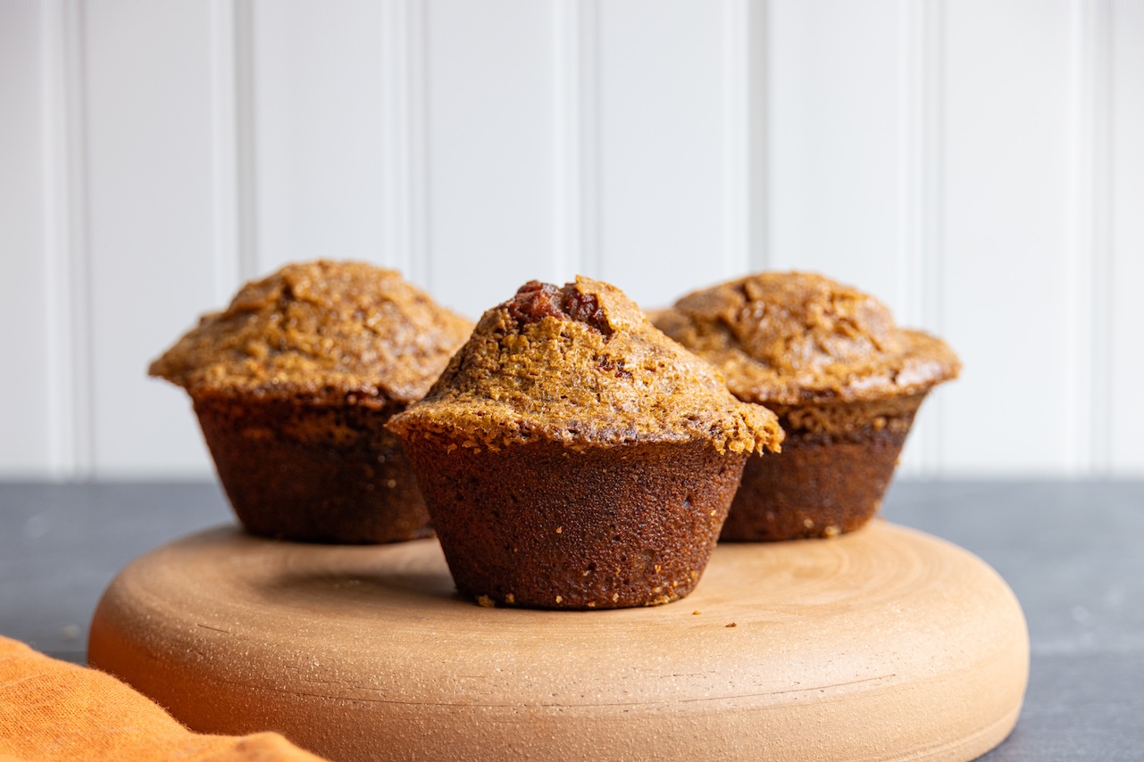 A trio of freshly baked pumpkin muffins on a wooden platter.
